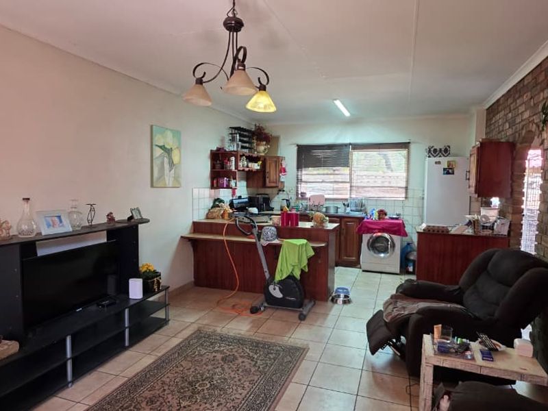 Open plan living and kitchen area featuring tiled floors, an exposed brick feature wall, and a functional kitchen layout with a breakfast bar.