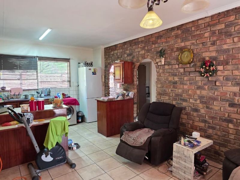 Open plan kitchen and living area featuring a prominent exposed brick wall, tiled flooring, and functional kitchen cabinetry with an archway leading to other rooms.