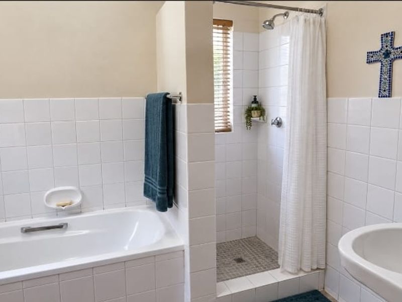 A functional bathroom featuring a built-in bathtub, separate shower enclosure, and a pedestal basin with white wall tiling.