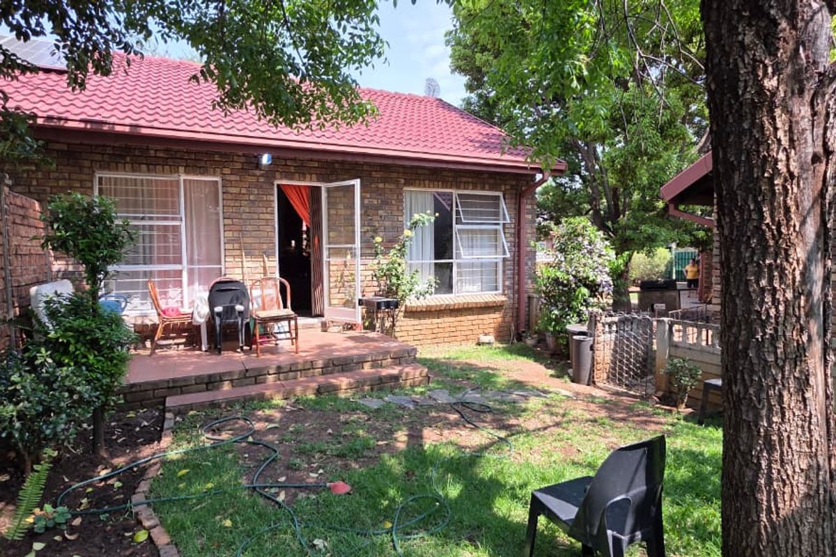 Rear view of a brick house featuring a tiled roof, paved patio area, and established garden space.