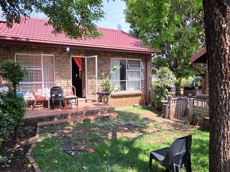 Rear view of a brick house featuring a tiled roof, paved patio area, and established garden space.