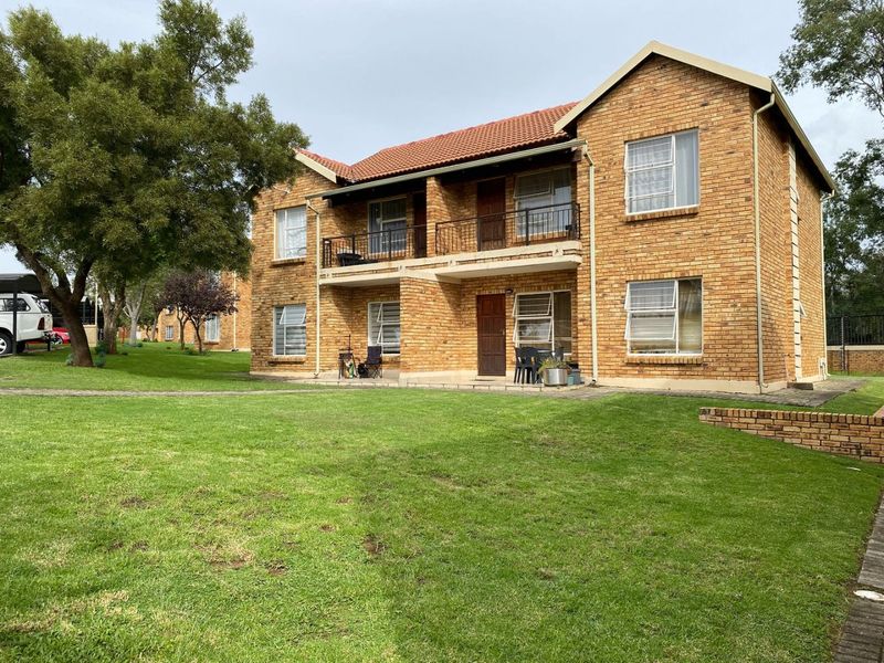 A view of the rear elevation of a face brick apartment building featuring a balcony, paved patio, and surrounding communal garden space.