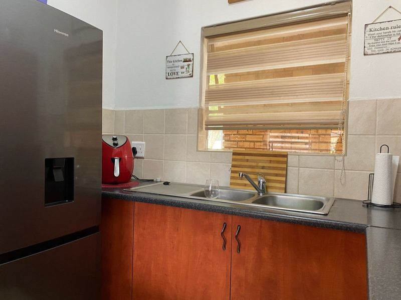 A functional kitchen area featuring timber veneer cabinetry, a double bowl stainless steel sink, and tiled splashback with a window for natural light.