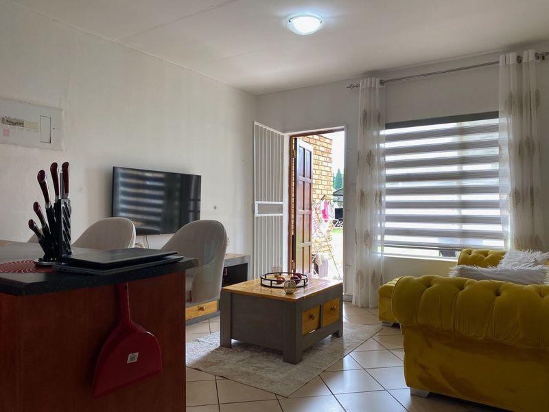 Open plan living area featuring tiled flooring, modern zebra blinds, and direct access to an outdoor space through a security gate.