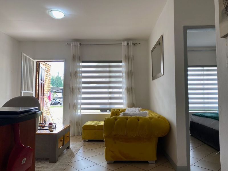 A living area featuring tiled flooring, zebra blinds, and direct access to the exterior, providing a functional and well-lit space.