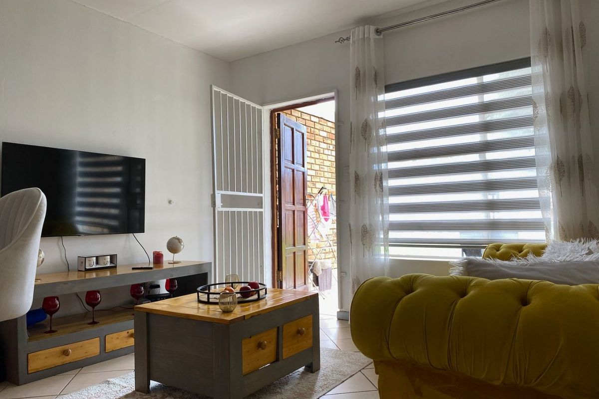A bright living room featuring tiled flooring, zebra blinds, and direct access to an outdoor area through a secure timber door.