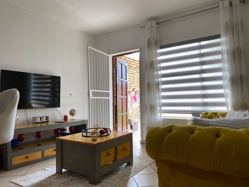 A bright living room featuring tiled flooring, zebra blinds, and direct access to an outdoor area through a secure timber door.