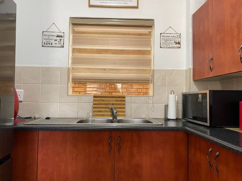 A functional kitchen area featuring laminate cabinetry, a dark laminate countertop, a stainless steel double sink, and a tiled splashback.