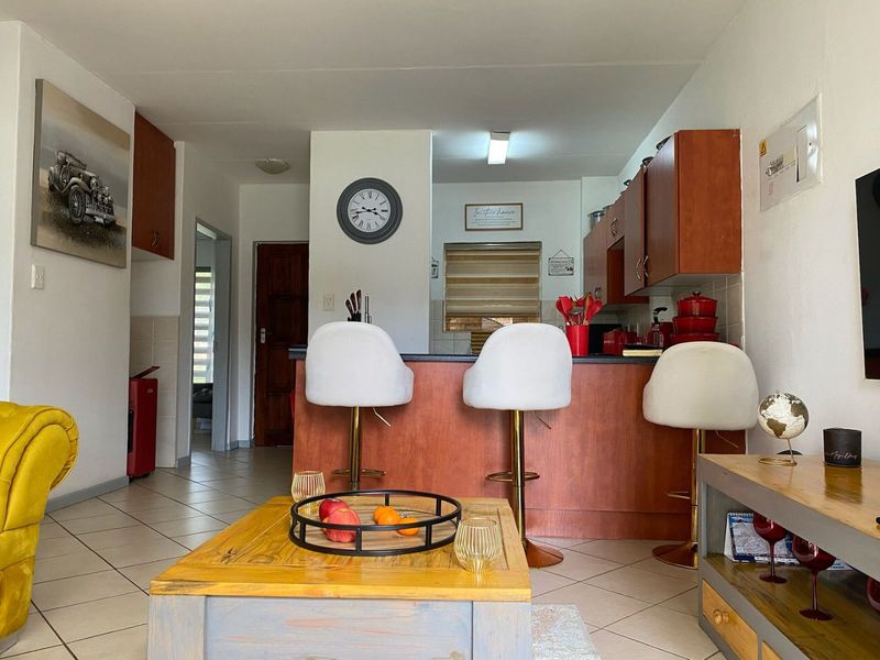 Open-plan living area featuring a kitchen with wooden cabinetry and a breakfast bar, seamlessly connected to the main living space with tiled flooring.