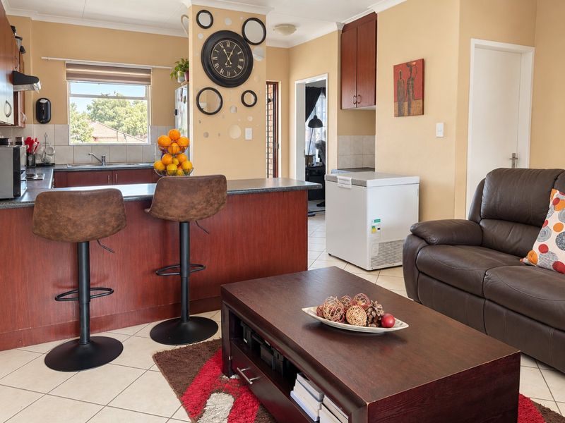 Open plan living area featuring a functional kitchen with dark wood cabinetry, laminate countertops, and tiled flooring, seamlessly connecting to the lounge space.