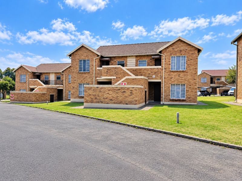A well-maintained multi-unit residential building featuring a face brick facade, tiled roof, and paved driveway with surrounding lawn.