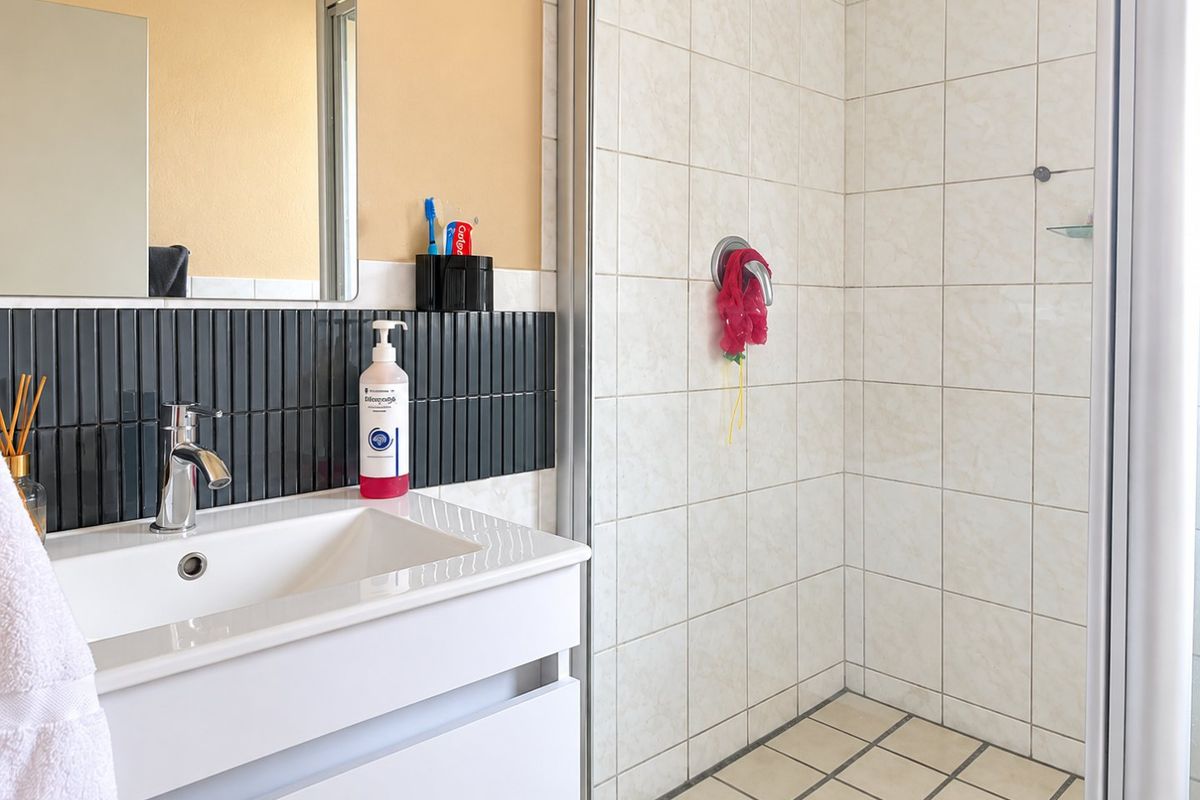 A functional bathroom featuring a modern vanity basin with mixer tap, a tiled shower enclosure, and a wall-mounted mirror.