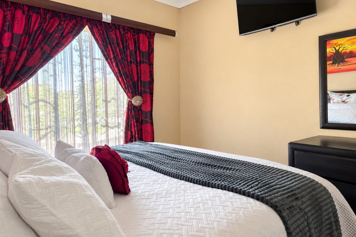 A well-maintained bedroom featuring neutral wall tones, a wall-mounted television, and decorative window treatments.