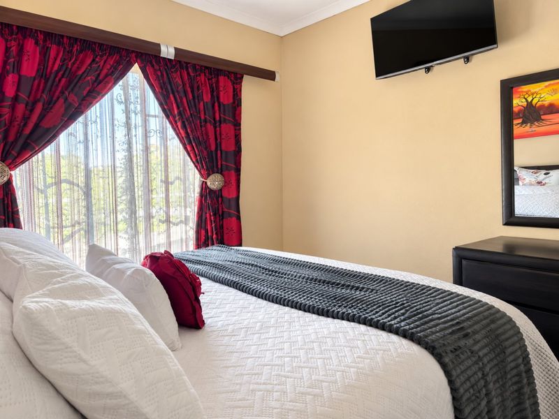 A well-maintained bedroom featuring neutral wall tones, a wall-mounted television, and decorative window treatments.