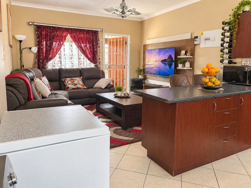 Open-plan living area featuring a kitchen island with dark cabinetry, tiled flooring, and a built-in media wall, creating a functional and connected living space.