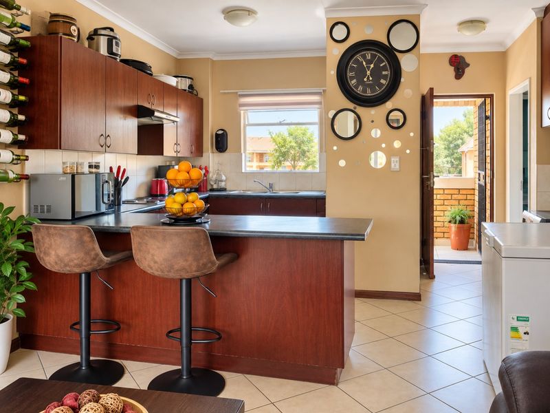 A functional kitchen featuring dark wood-look cabinetry, laminate countertops, a breakfast bar, and tiled flooring with direct access to an outdoor area.