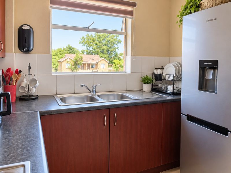 A functional kitchen area featuring a double bowl stainless steel sink, laminate countertops, tiled splashback, and built-in cabinetry with a window view.