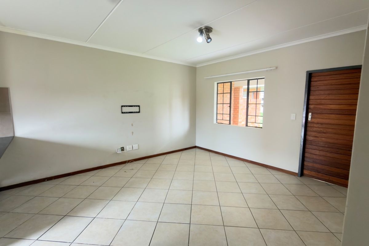 An empty living room featuring tiled flooring, a timber door, and a window with security bars, ready for personalization.
