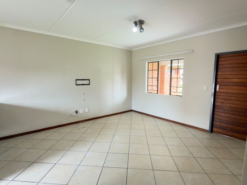 An empty living room featuring tiled flooring, a timber door, and a window with security bars, ready for personalization.