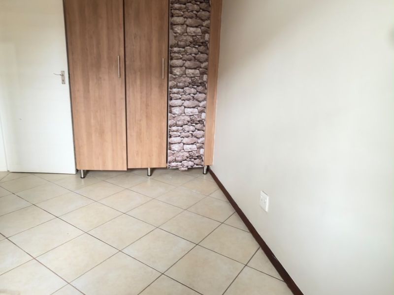 A clean, empty bedroom featuring neutral tiled flooring and a built-in wardrobe with wood-grain finish and decorative stone-effect paneling.