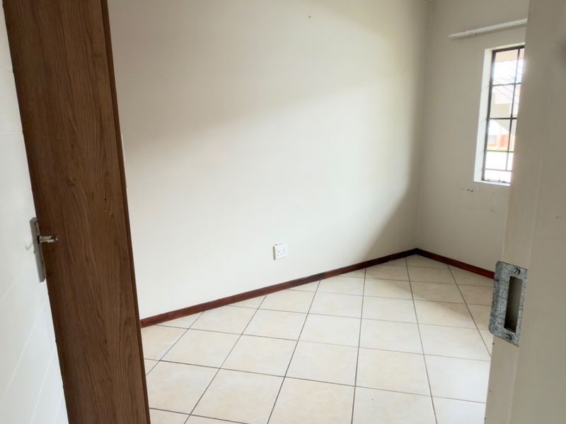 A clean, empty bedroom featuring neutral tiled flooring, a window with security bars, and a simple ceiling light fixture.
