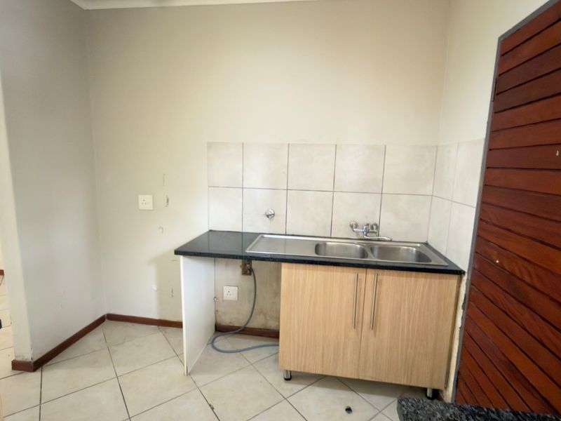 A functional scullery area featuring a double bowl stainless steel sink, granite countertop, and tiled splashback, currently in need of minor cosmetic updates.