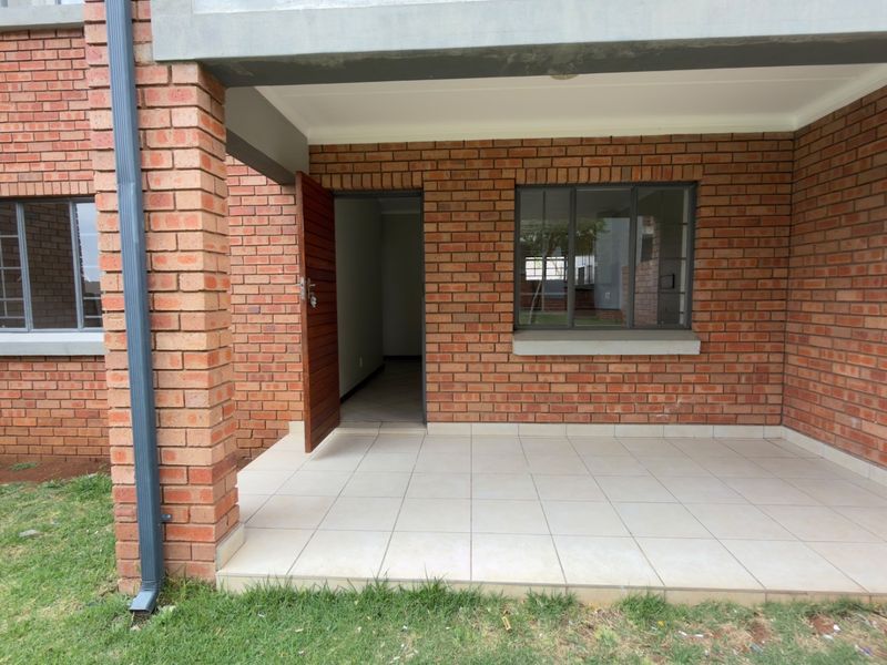 A covered patio area featuring exposed brickwork, tiled flooring, and direct access to the apartment interior through a standard door.