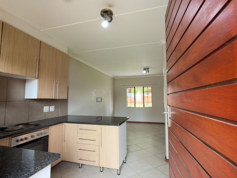 Open-plan kitchen and living area featuring light wood cabinetry, granite countertops, built-in oven and hob, and neutral tiled flooring throughout.