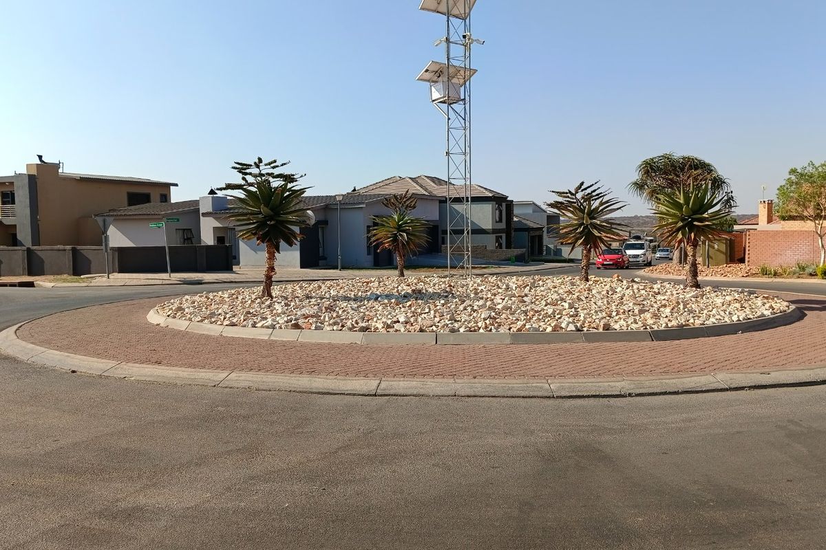 A view of a residential street roundabout featuring a central landscaped island with a telecommunications mast and solar panels.