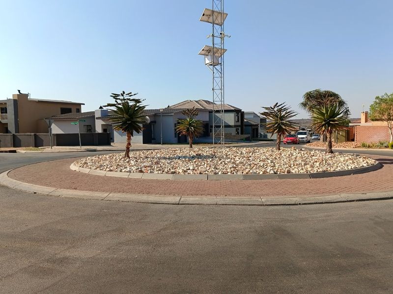 A view of a residential street roundabout featuring a central landscaped island with a telecommunications mast and solar panels.