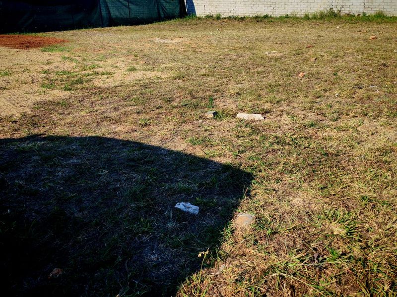 A vacant residential plot featuring a boundary wall and temporary shade cloth fencing, ready for development.
