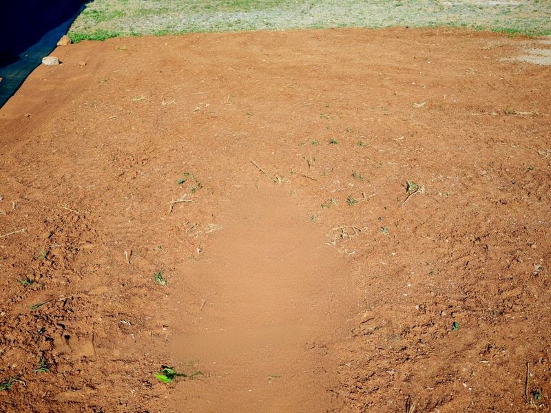 A view of a vacant residential plot featuring cleared earth and a perimeter boundary wall.