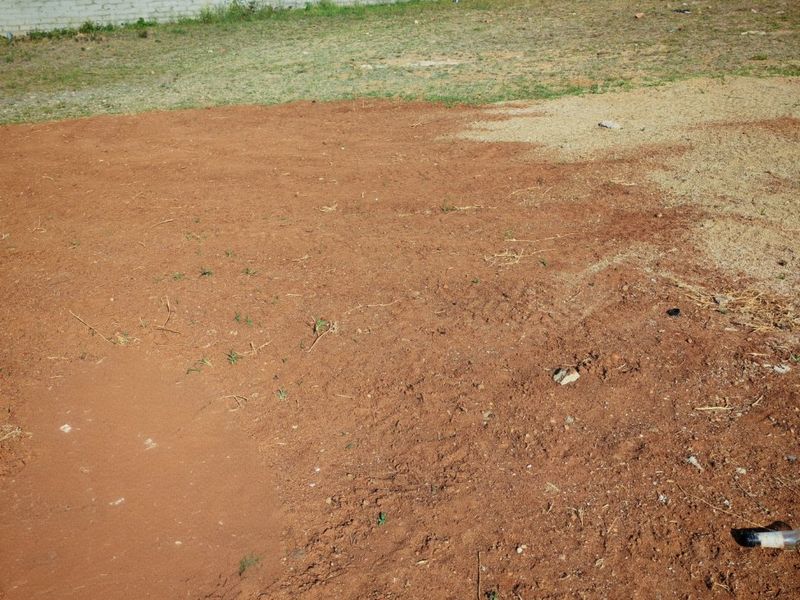 A view of a vacant residential plot featuring cleared earth and a perimeter boundary wall.