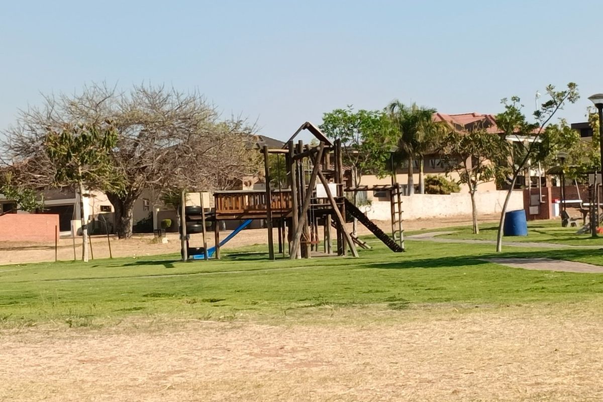 A communal garden area featuring a wooden playground structure set on a maintained lawn with paved pathways.