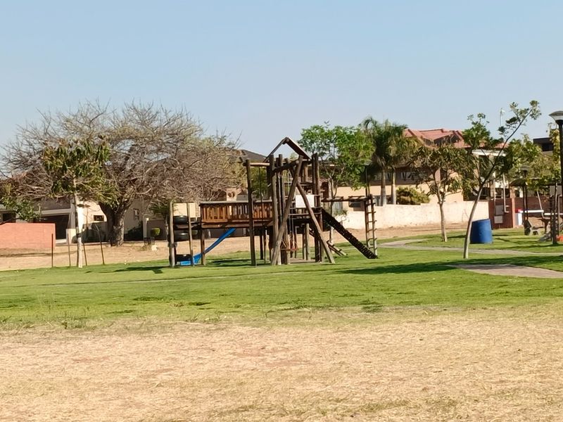 A communal garden area featuring a wooden playground structure set on a maintained lawn with paved pathways.