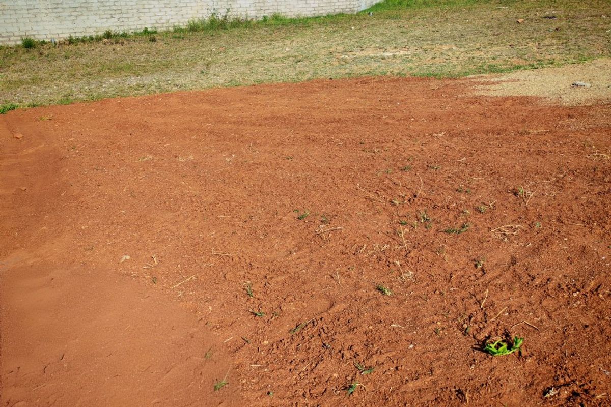 A view of a vacant residential plot featuring cleared soil and a perimeter boundary wall, situated in a developed neighborhood.