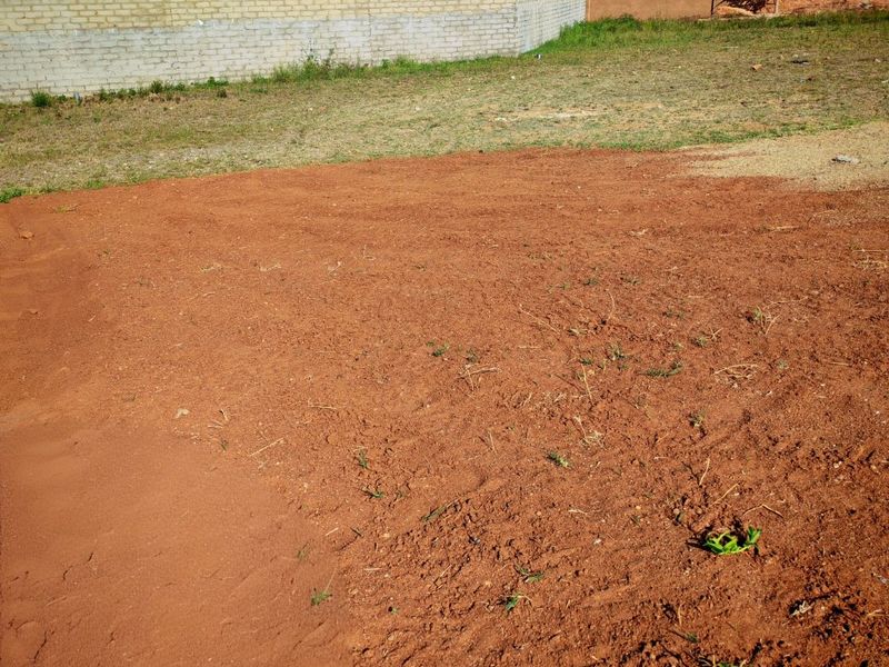 A view of a vacant residential plot featuring cleared soil and a perimeter boundary wall, situated in a developed neighborhood.