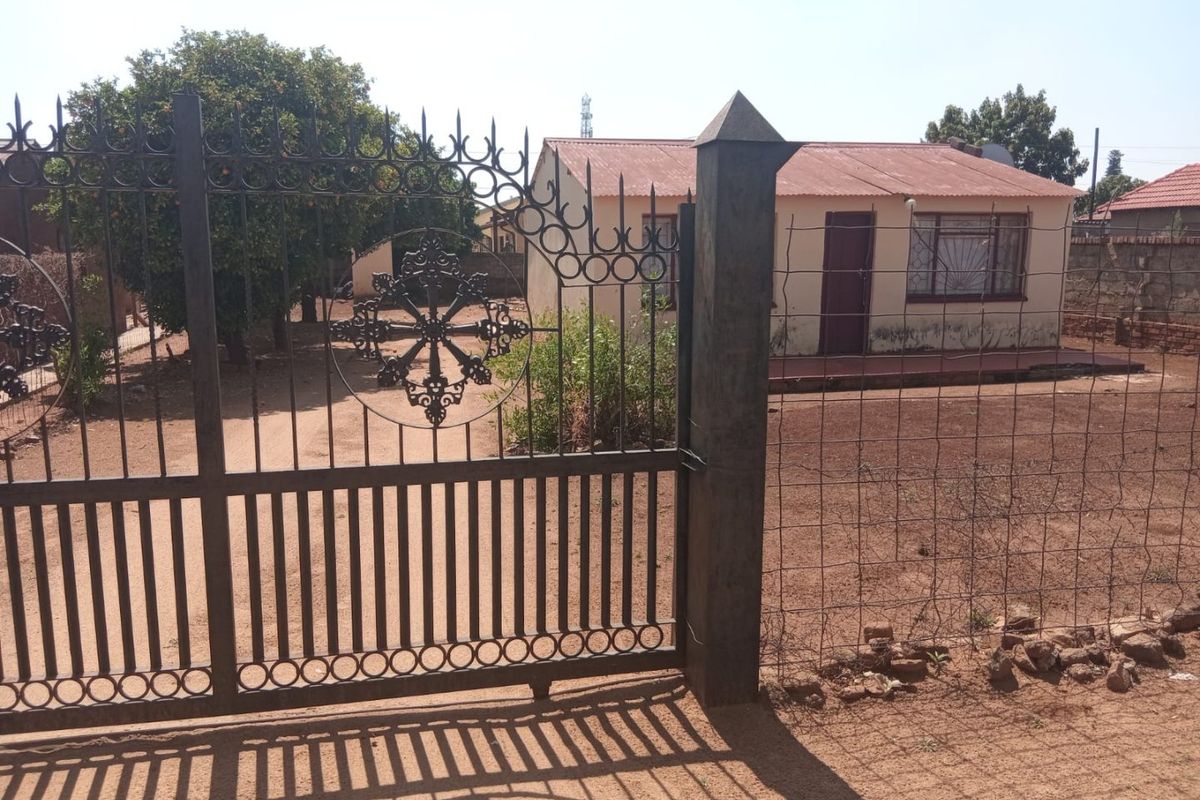 Front view of a single-story house featuring a decorative wrought iron gate, corrugated metal roof, and security bars on the windows.