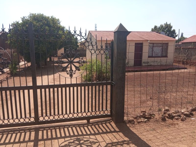 Front view of a single-story house featuring a decorative wrought iron gate, corrugated metal roof, and security bars on the windows.