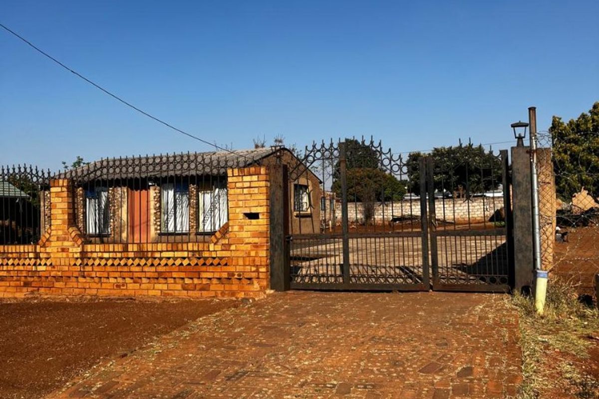 Front view of the property featuring a brick boundary wall, wrought iron security gate, and a paved driveway leading to the entrance.