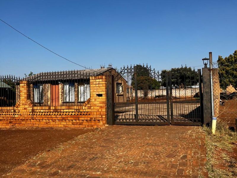 Front view of the property featuring a brick boundary wall, wrought iron security gate, and a paved driveway leading to the entrance.