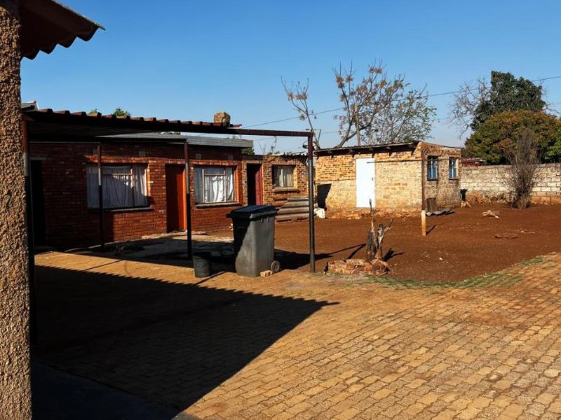 Rear exterior view of the property featuring exposed brick structures, a paved courtyard area, and a covered patio space.