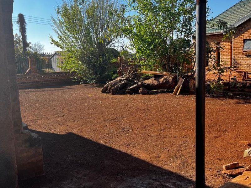 A rear yard area featuring a paved patio, brick boundary wall, and an unlandscaped garden space requiring maintenance and clearing.