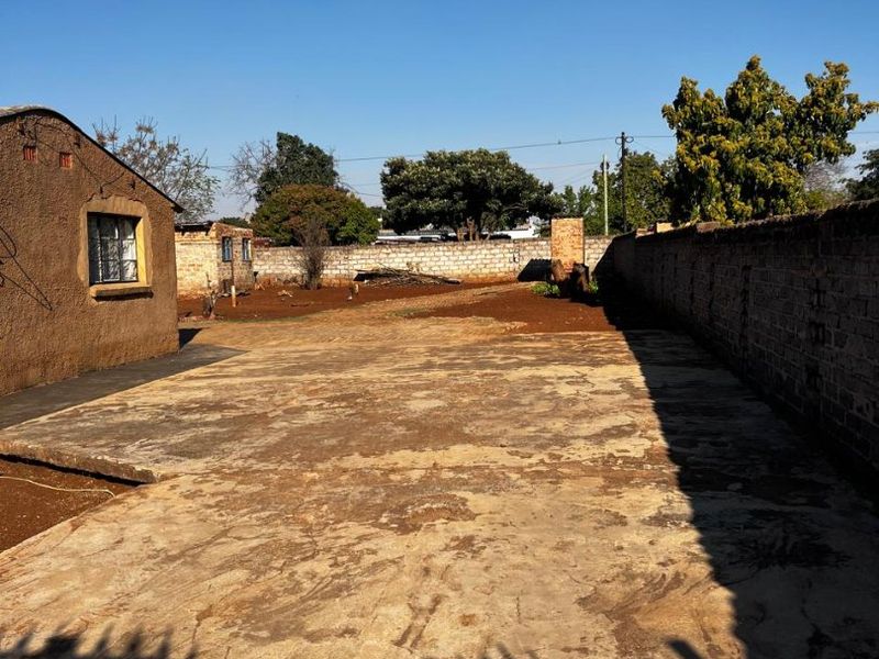 Spacious rear yard featuring a large concrete driveway, enclosed by perimeter brick walls and a metal gate, offering potential for landscaping or development.