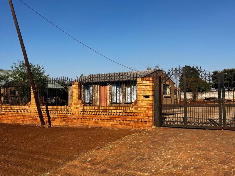 Front view of a property featuring a face brick boundary wall, wrought iron security fencing, and a paved driveway entrance.