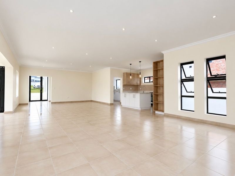 Spacious open-plan living and kitchen area featuring neutral tiled flooring, modern cabinetry, recessed lighting, and large windows providing ample natural light.