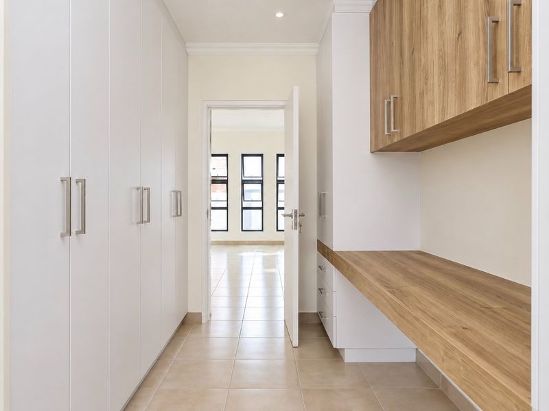 A clean, modern utility or study area featuring extensive built-in white cabinetry, a wood-look countertop, and neutral tiled flooring.