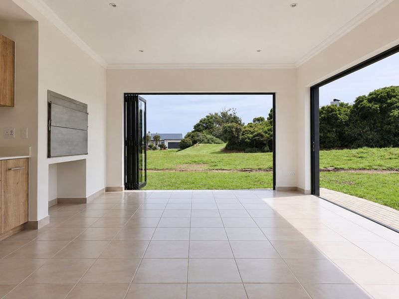 Spacious open-plan living area featuring tiled floors, built-in cabinetry, a built-in braai, and large bi-fold doors opening to a garden view.