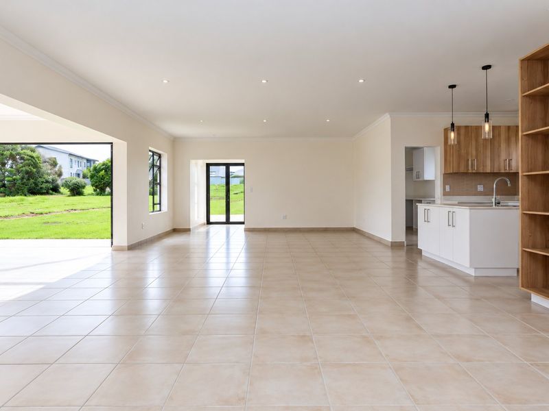 Spacious open-plan living and kitchen area featuring neutral tiled floors, modern cabinetry, built-in shelving, and seamless access to the outdoor garden through large glass doors.