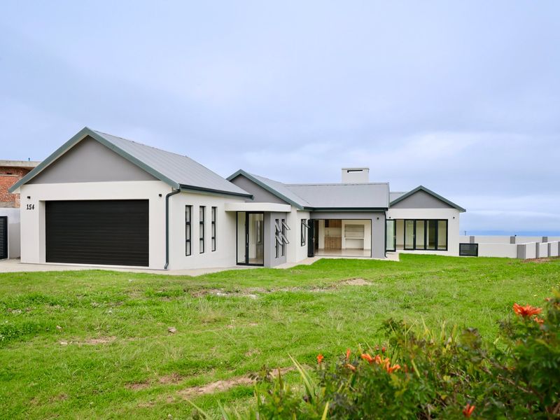 A modern single-story residential home featuring a double garage, neutral exterior finish, metal roofing, and large windows set on a landscaped plot.
